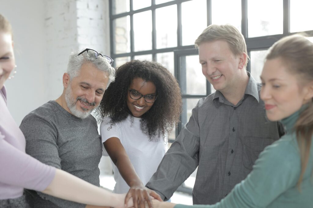 A diverse group of colleagues smiling and putting hands together indoors in a bright office.